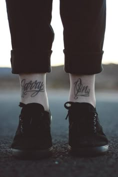 a person with tattoos on their feet standing in the middle of an asphalt road wearing black shoes