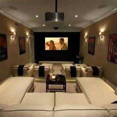 a home theater with couches and tables in front of the projector screen that is turned on