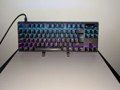 a computer keyboard with blue and purple lights on it's side, sitting on a table