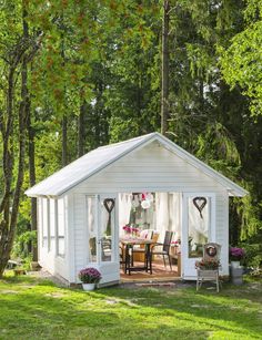 a small white shed sitting on top of a lush green field next to a forest