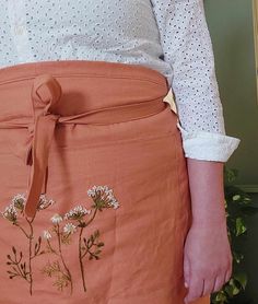 a woman wearing an orange skirt with white flowers on the side and a brown belt around her waist