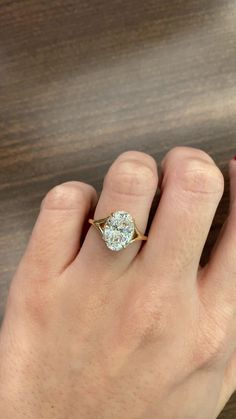 a person's hand holding a ring with a diamond in it on top of a wooden table