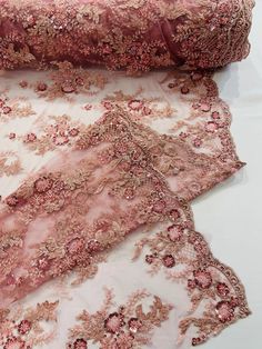 three pieces of pink and gold embroidered fabric on white cloth, one is folded over the other