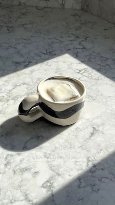 a white and black cup sitting on top of a marble counter next to a window