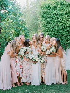 a group of women standing next to each other in front of some bushes and trees