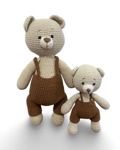 two crocheted teddy bears standing next to each other in brown overalls and holding hands