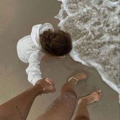 two people are standing on the beach with their feet in the water and one is wearing a white shirt