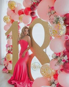 a woman in a pink dress standing next to a giant number and balloon backdrop with flowers