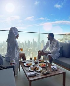 two people in white robes toasting at a table with food and drinks on it