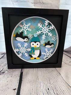 an ornament with penguins and snowflakes on it in a black frame