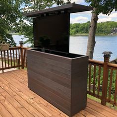 an outdoor entertainment center on a deck next to the water with trees in the background