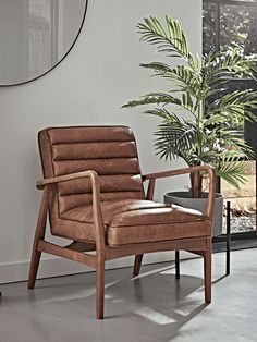 a brown chair sitting next to a potted plant in front of a wall mounted mirror