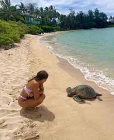 a woman kneeling down next to a turtle on a beach