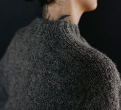 a close up of a woman's neck wearing a gray sweater and black hair