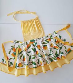 a yellow apron with oranges and green leaves on it, sitting next to a white background