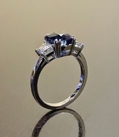 "DeKara Designs Collection Beautiful Modern/Art Deco Ceylon Blue Sapphire and Diamond Ring Metal- 90% Platinum, 10% Iridium Stones- Genuine Cushion Cut Ceylon/Sri Lanka Royal Blue Sapphire 2.87 Carats. Two Trapezoid Cut Diamonds G-H Color VS1 Clarity 0.93 Carats. Size-6. FREE SIZING Entirely Handmade, Classic and Timeless Art Deco Inspired Ceylon Cushion Cut Royal Blue Sapphire Diamond Engagement Ring. This ring is out of this world with the center Ceylon Sapphire being exceptional in quality, c Luxury Blue Sapphire Ring With Asscher Cut, Luxury Blue Sapphire Ring Asscher Cut, Blue Asscher Cut Sapphire Ring In Luxury Style, Platinum Blue Sapphire Gemstone Ring, Blue Sapphire Gemstone Ring In Platinum, Gia Certified Blue Sapphire Ring In Platinum, Blue Diamond Ring Emerald Cut, Blue Diamond Emerald Cut Ring, Blue Sapphire Three Stone Ring With Diamonds