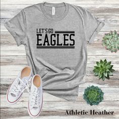 Get ready to soar with our "Let's Go Eagles" T-shirt! Perfect for students, teachers, alumni, and fans, this tee is the ultimate way to rally behind your team and show your Eagle pride. This classic unisex jersey short sleeve tee fits like a well-loved favorite. Soft cotton and quality print make users fall in love with it over and over again.  .: 100% Airlume combed, and ring spun cotton (fiber content may vary for different colors) .: Light fabric (4.2 oz/yd² (142 g/m .: Retail fit .: Tear away label .: Runs true to size CARE INSTRUCTIONS Wash item inside out in cold water Do not bleach Do not dry clean Do not iron directly on the design. Tumble dry low. NOTE: All apparel items from Chosen Chic are Direct to Garment printing which means the design is print into the fibers of that fabric Game Day T-shirt With Team Name In Athletic Heather, Athletic Heather T-shirt With Team Name For Game Day, Athletic Heather T-shirt For Game Day, Athletic Heather T-shirt For Sports Season Fan Merchandise, Pre-shrunk Athletic Heather T-shirt For Game Day, Sporty Athletic Heather T-shirt For Game Day, Sporty T-shirt In Athletic Heather For Game Day, Fan Apparel T-shirt For Athletic Heather, Athletic Heather T-shirt With Team Logo