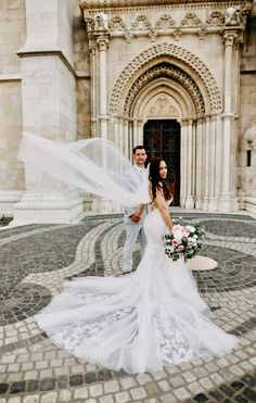 a bride and groom standing in front of an old building with a veil blowing in the wind