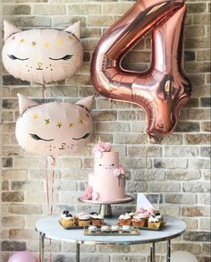 a table topped with pink and gold balloons next to a wall covered in cat decorations