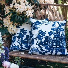 two blue and white pillows sitting on top of a wooden bench next to some flowers