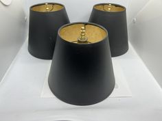 three black lamps are sitting on a white surface with gold trim around the top and bottom