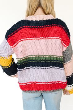 This sweater is a striking example of a chunky, hand-knit garment featuring a patchwork-like design with bold, contrasting colors. The sweater is made from thick yarns, creating a warm and cozy feel that is ideal for colder weather. It has a high, slightly ribbed neckline, which adds to the snug, comfortable look of the piece.

The design is characterized by wide, horizontal stripes in a variety of colors, including pastel pink, deep blue, lavender, mustard yellow, forest green, and bold red.