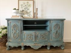 an old blue painted entertainment center with ornate carvings on the doors and drawers, next to a potted plant