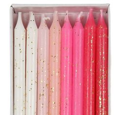 pink and white candles are lined up in a box with gold confetti on them