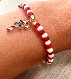 a red and white beaded bracelet on someone's arm with a cross charm