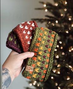 a hand holding three crocheted items in front of a christmas tree