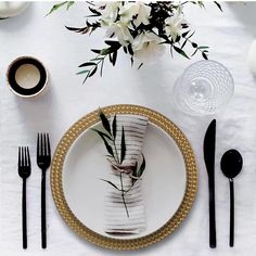 a white table setting with black and gold place settings, silverware, and flowers