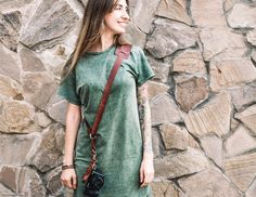 a woman standing in front of a stone wall with a camera strap around her neck