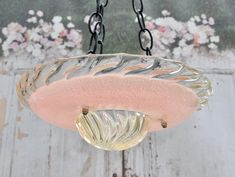 a glass light hanging from a chain on a wooden wall with flowers in the background