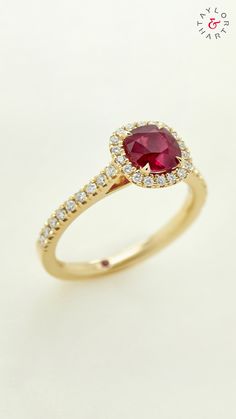 a gold ring with a red stone surrounded by white diamonds on a white background,