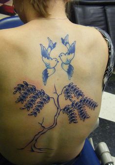 the back of a woman's shoulder with blue birds and tree tattoos on it