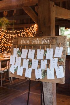 a wooden sign with seating cards attached to it in front of a string of lights