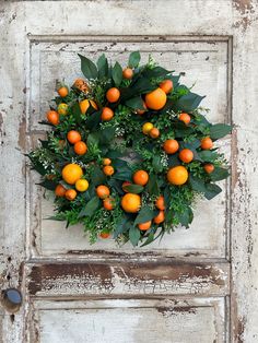 an orange wreath on the front door of a house with green leaves and flowers around it