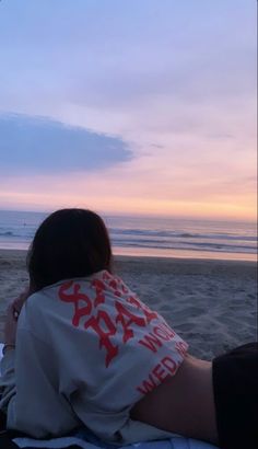 a woman sitting on top of a beach next to the ocean at sunset or dawn