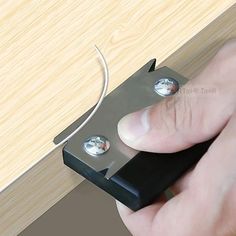 a hand is holding a piece of metal in front of a wooden table with two magnets on it