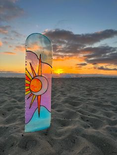 a surfboard sitting on top of a sandy beach under a cloudy sky at sunset