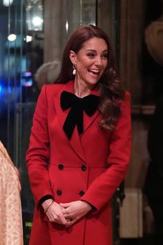 a woman in a red coat and black bow tie smiles as she stands next to another woman