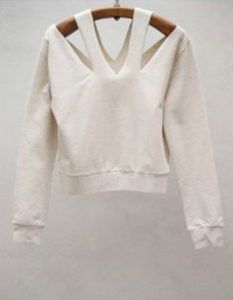 a white sweater with cut out shoulders hanging on a hanger in front of a wall