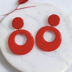 Handmade from polymer clay, these vibrant red open circle hoop dangle earrings make a bold and stylish statement. Coated with resin on both sides for a glossy finish, these retro oversized drop earrings are a timeless and fashionable accessory. This classic style has been popular across the decades, from the 50s to the 90s and beyond. Treat yourself to a pair or surprise a friend with a gift. The hoops are adorned with gold tone posts and jump rings. Hoop Dangle Earrings, Retro Gift, The 50s, Unique Handmade Jewelry, Earrings Statement, The 90s, Vibrant Red, Jump Rings, Handmade Earrings