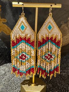 the beaded earrings are hanging from a hook on a gold plated display stand