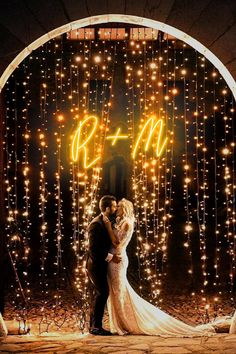 a bride and groom standing in front of a backdrop with lights that spell out the word b & m