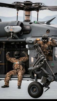 two men in camouflage sit on the wing of an aircraft while another man stands next to it