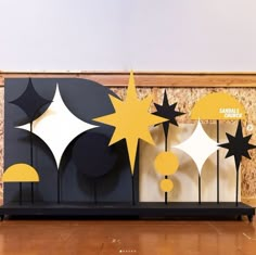 an art piece with yellow and black stars on it in front of a wooden wall