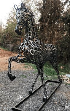 a metal horse statue sitting on top of a gravel ground next to trees and bushes