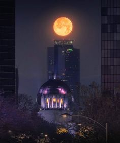 the full moon is seen over a building in this cityscape photo taken at night