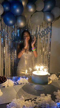 a woman standing in front of a cake with candles on it and balloons behind her